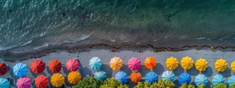 Aerial view of colorful beach umbrellas lining a sandy shore, emphasizing vibrant hues and the ocean's edge, relevant to local business visibility and engaging online presence.